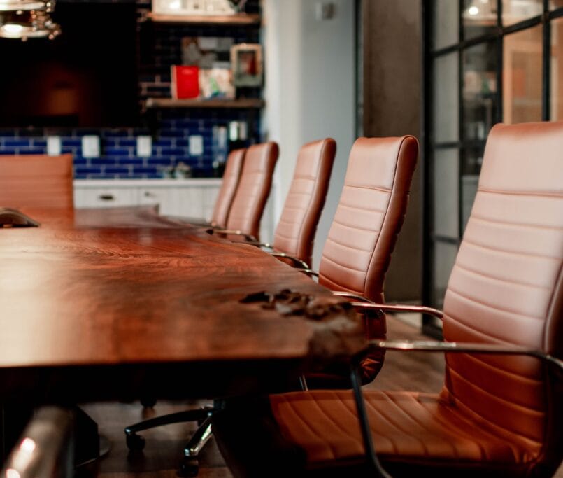 Une salle de réunion élégante avec une longue table en bois massif et des chaises en cuir marron, idéale pour des réunions d'affaires professionnelles